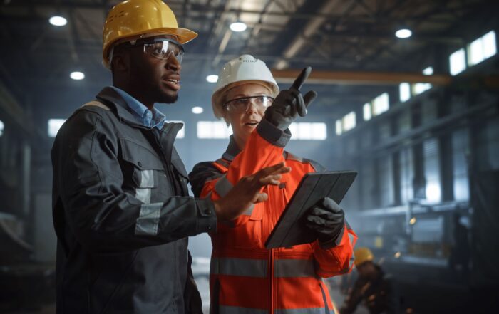 Two Heavy Industry Engineers Stand in Steel Metal Manufacturing Factory, Use Digital Tablet Computer and Have a Discussion