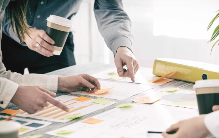 A close-up of a group of people collaborating around a table, pointing to various documents and sticky notes.