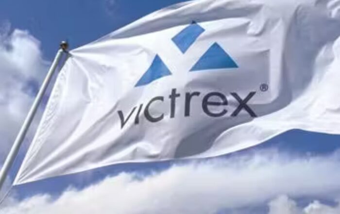 White flag with the Victrex logo flying against a bright blue sky with scattered clouds.