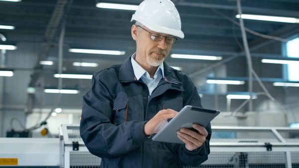 Maintenance engineer using a tablet on the shop floor wearing a safety helmet.