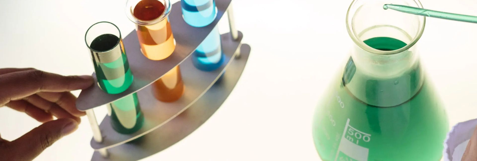 Scientist with pipette transferring green liquid into flask with colorful test tubes.