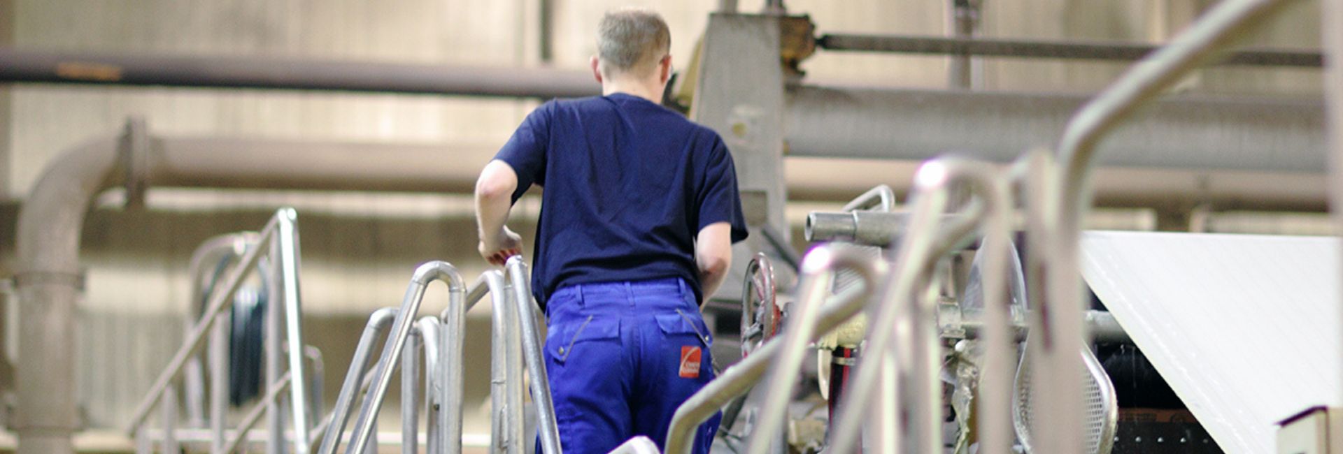 Maintenance technician walking up industrial equipment stairs inside a production facility.