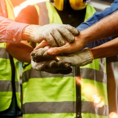 Team of workers in safety vests and gloves stacking hands to show teamwork.
