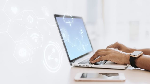 Person typing on a laptop with digital icons floating around and a smartphone nearby