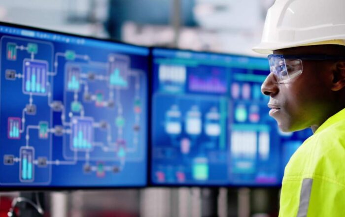 Industrial professional in safety gear monitoring digital process dashboards in a control room.